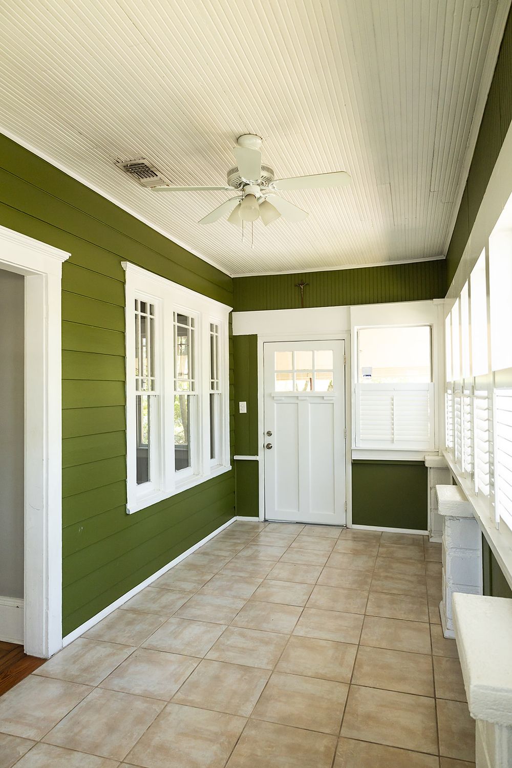 Empty enclosed porch interior with olive green walls, white trim, and beige tiled flooring in a traditional home.