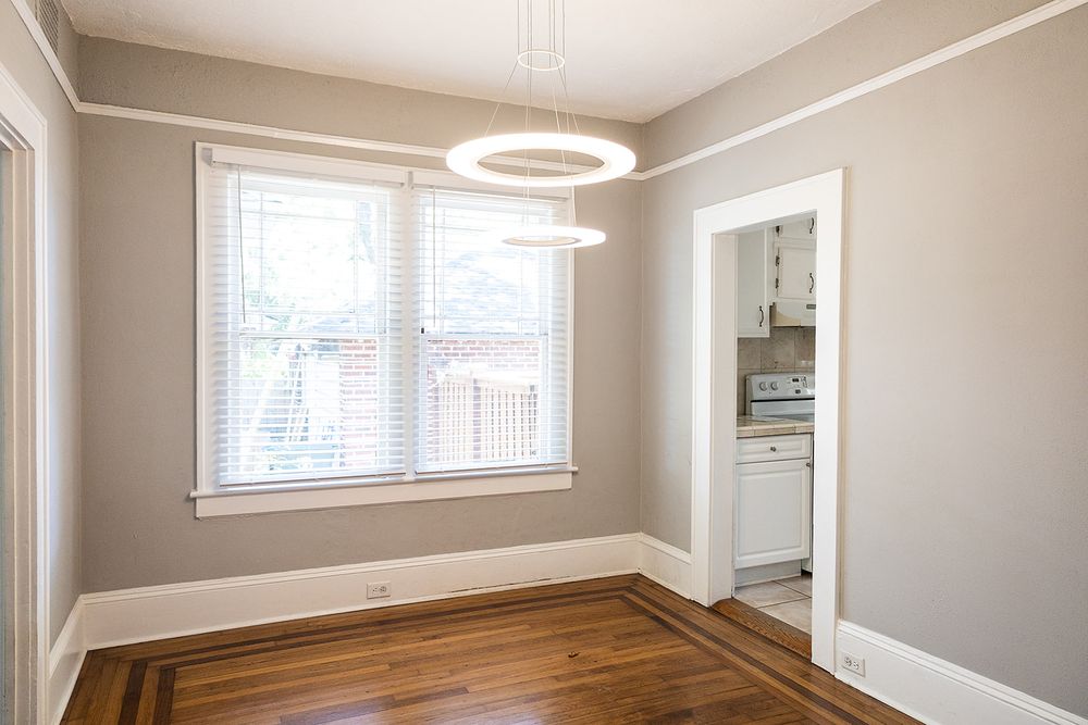 Modern bedroom features gray walls, hardwood flooring, and a contemporary circular ceiling light fixture with large windows.