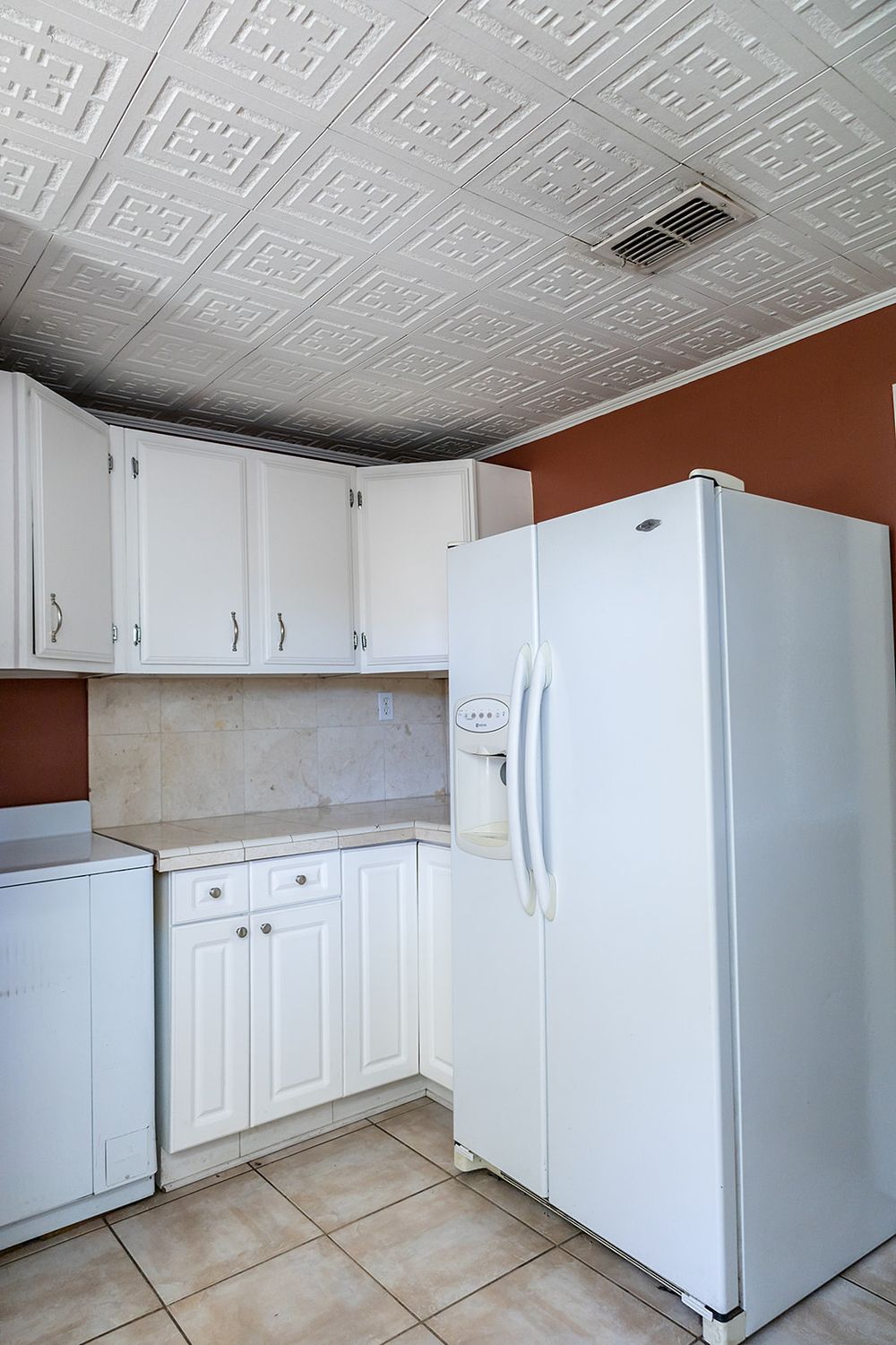 White kitchen cabinets with decorative ceiling tiles and wood floors in an empty residential space.