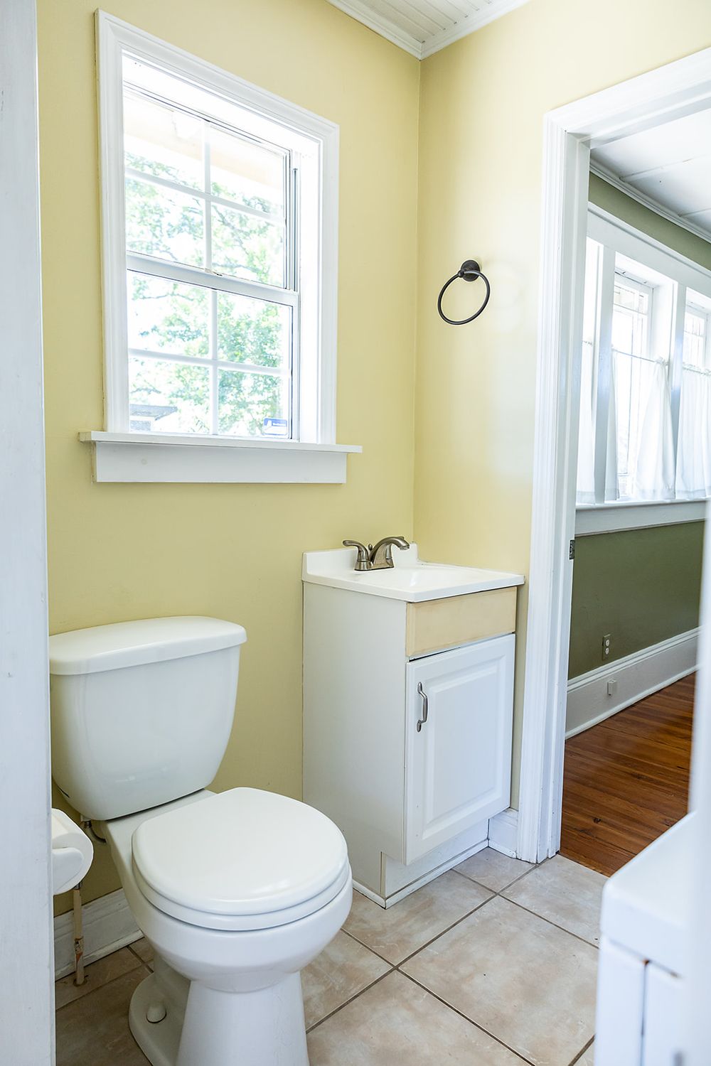 A bright, airy bathroom with pale yellow walls, white trim, hardwood floors, and multiple windows offering natural light.