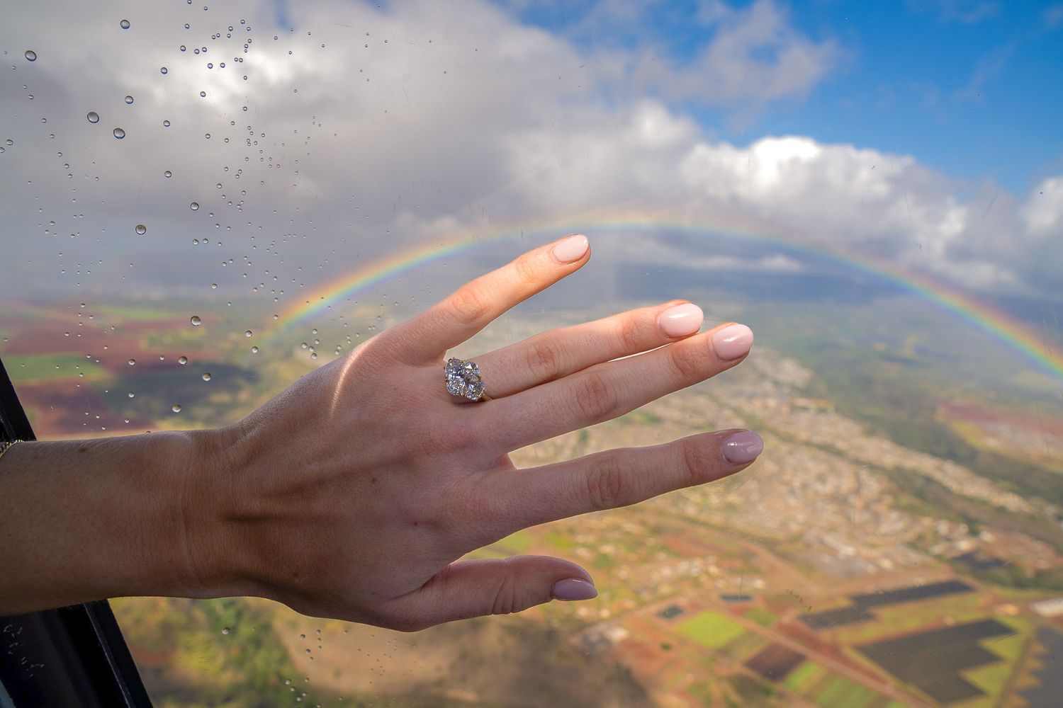 After proposal, bride reaches out towards a vibrant rainbow showing her new engagement ring arcing across Oahu landscape in the distance.