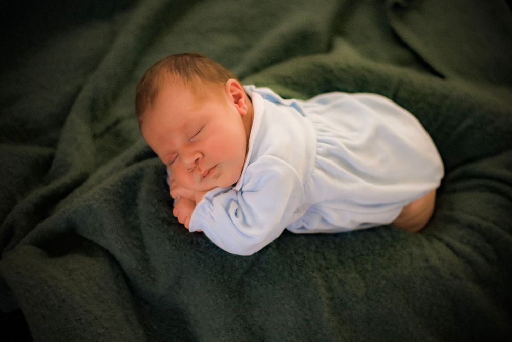 Sleeping infant in white clothes rests on dark green blanket.