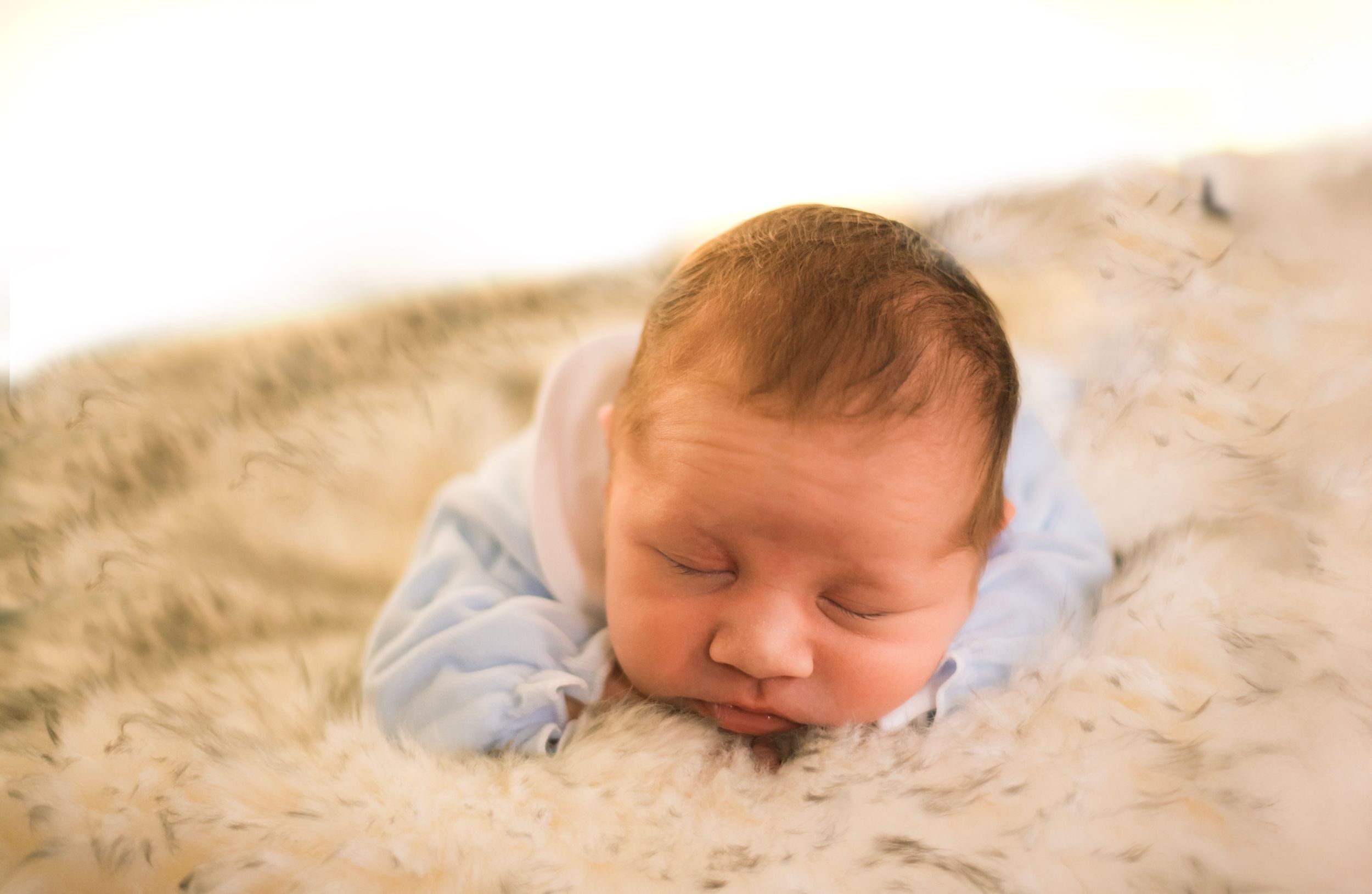Sleeping baby in light clothing rests on cream colored textured surface.