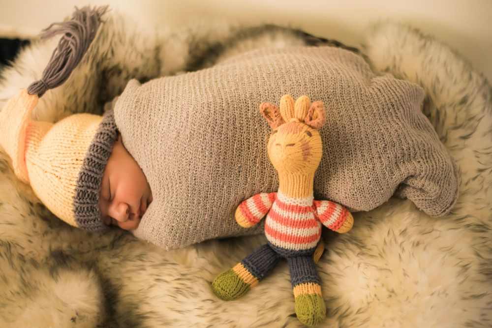 Sleeping newborn in knit outfit with stuffed giraffe toy on furry blanket.