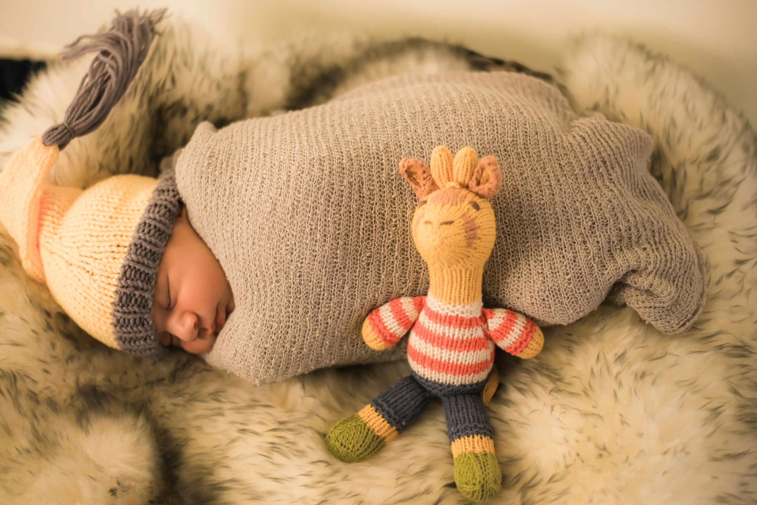 Sleeping newborn in knit outfit with stuffed giraffe toy on furry blanket.