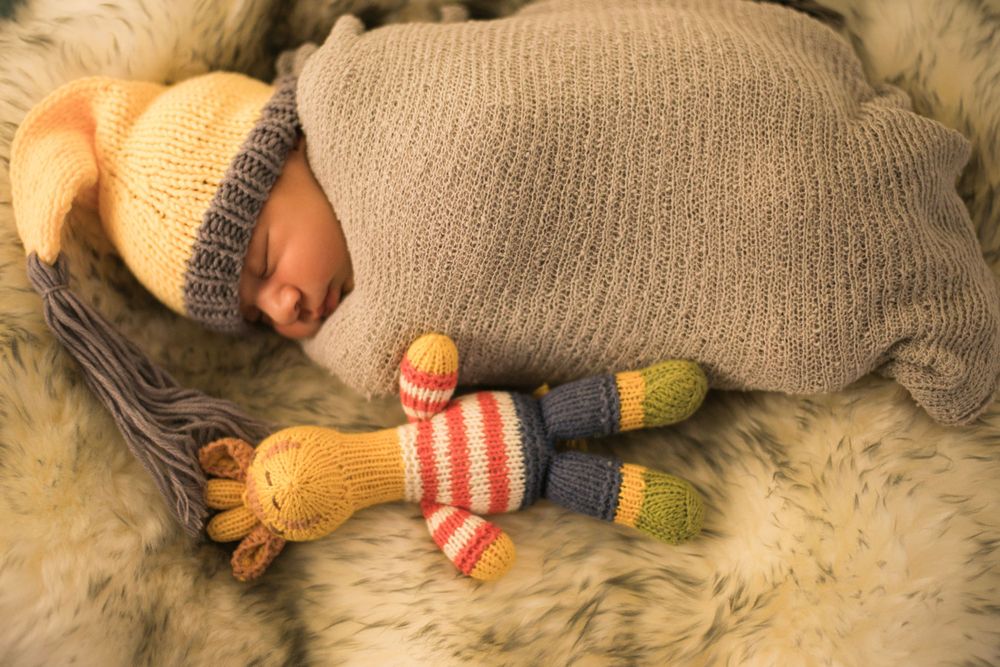 Cozy sleeping infant in knit wear with striped giraffe toy on soft fur blanket.