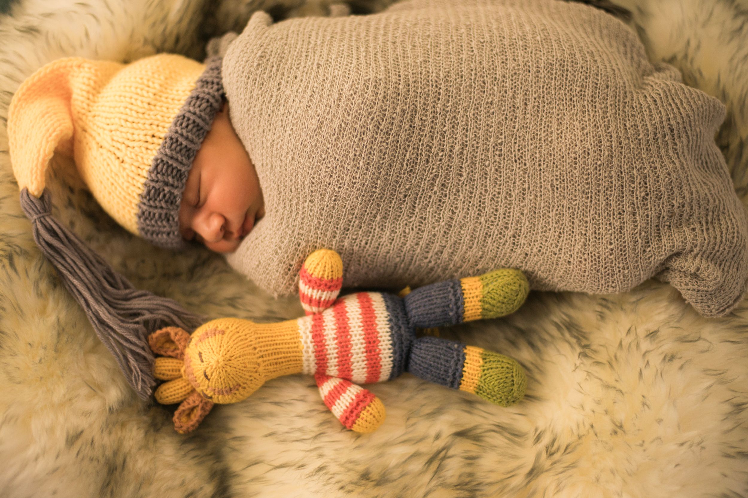Cozy sleeping infant in knit wear with striped giraffe toy on soft fur blanket.