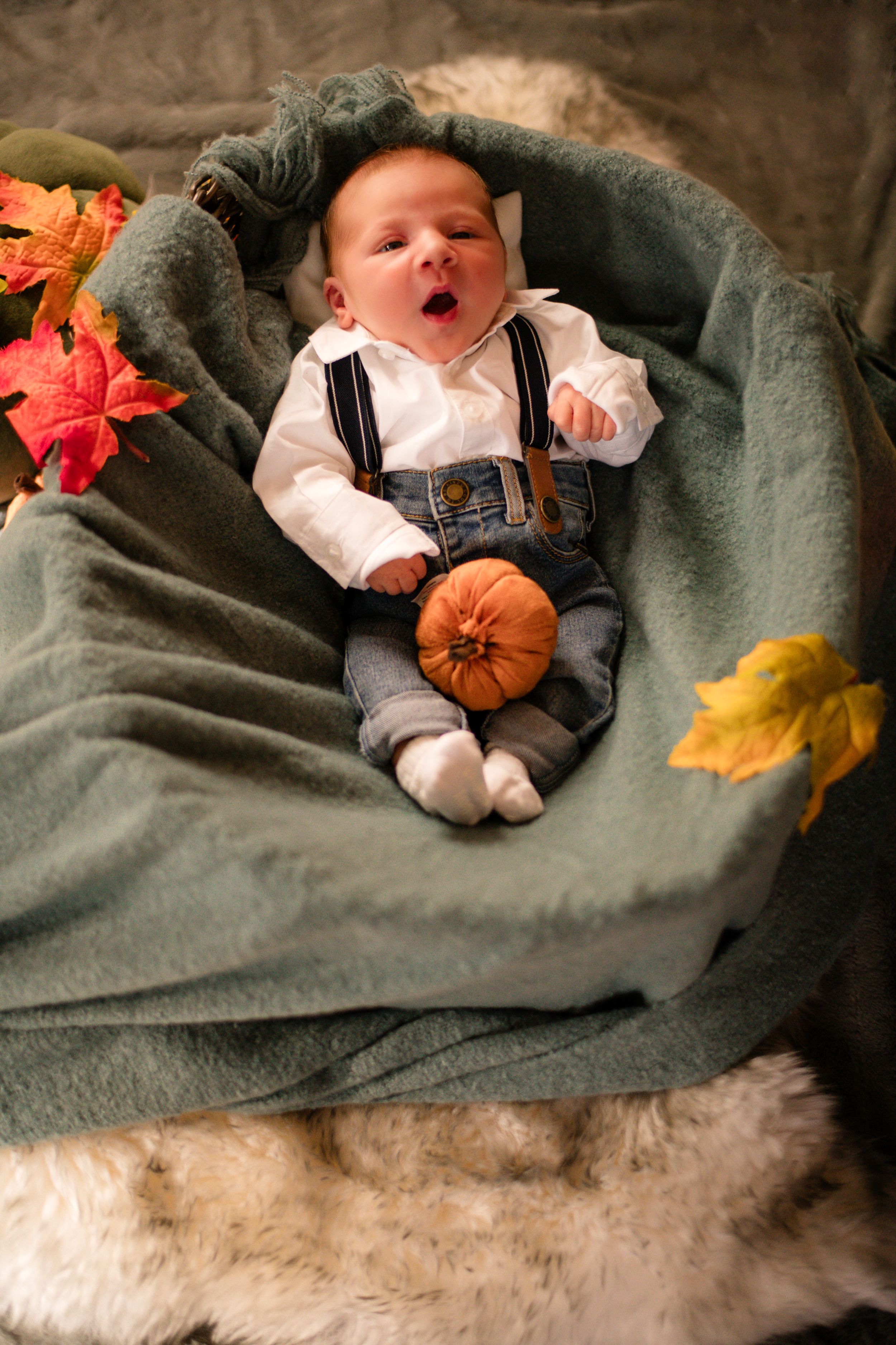 Autumn themed portrait of sleeping infant with pumpkin and fall leaves on gray blanket.