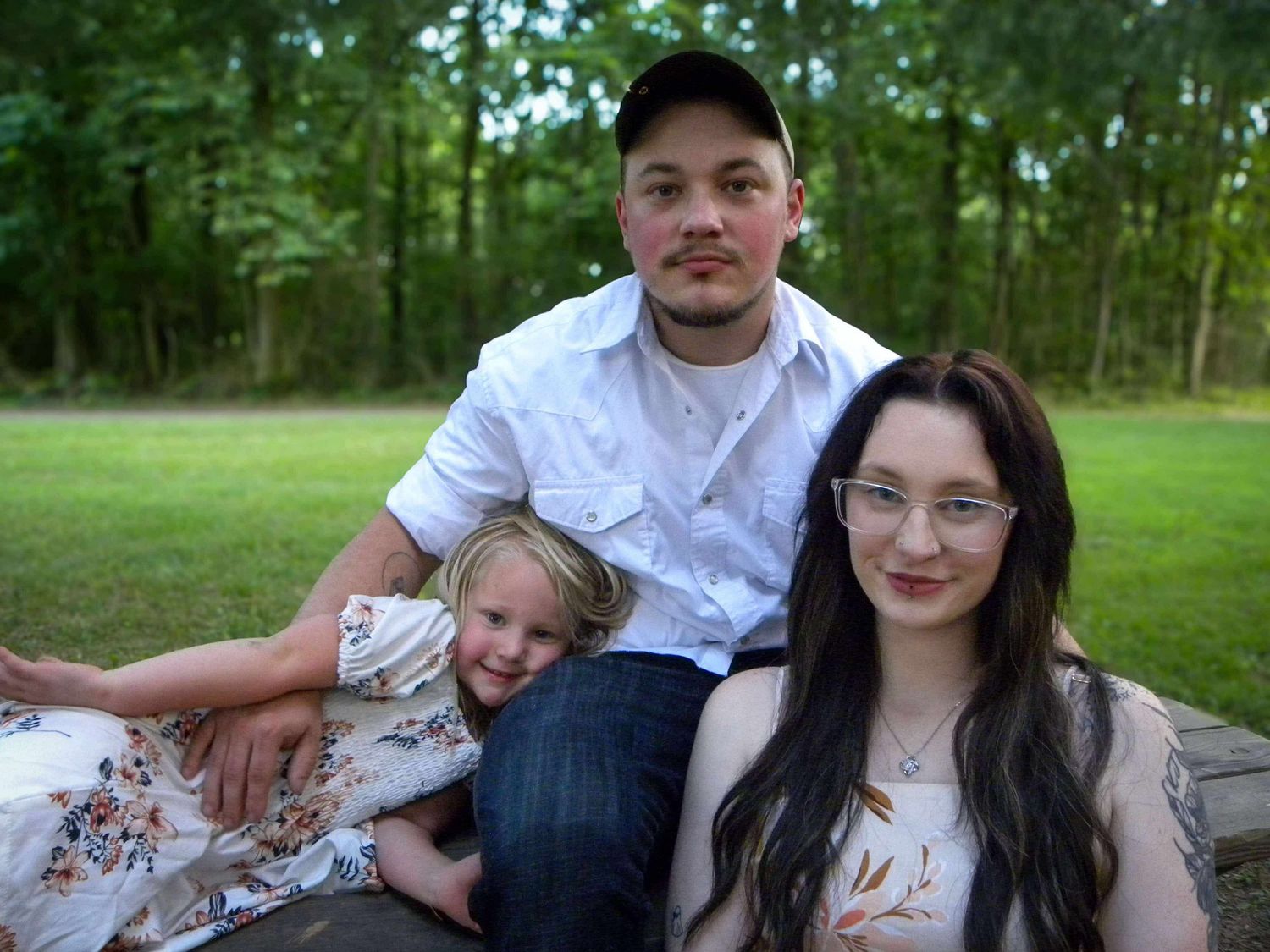 Family portrait outdoors in a grassy field with trees in the background.