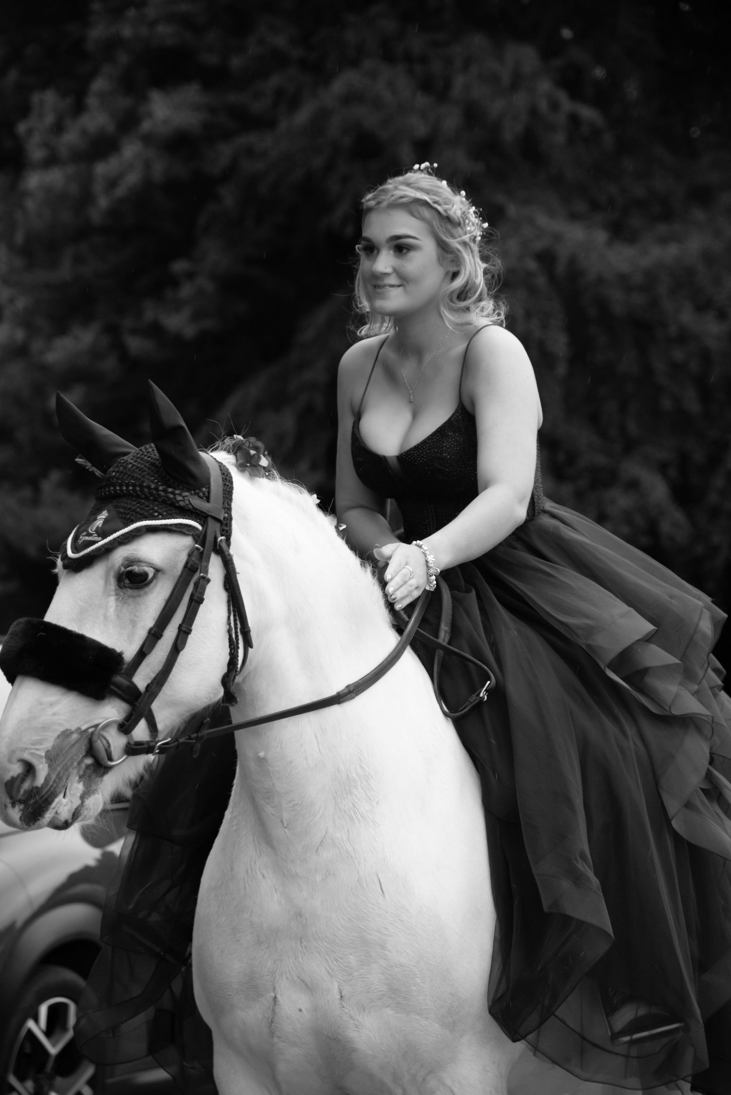 Elegant equestrian in black formal dress rides gracefully atop a majestic white horse in black and white photography.