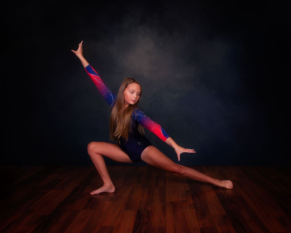 Graceful dancer performs contemporary dance movements in a dark studio with wooden floors.