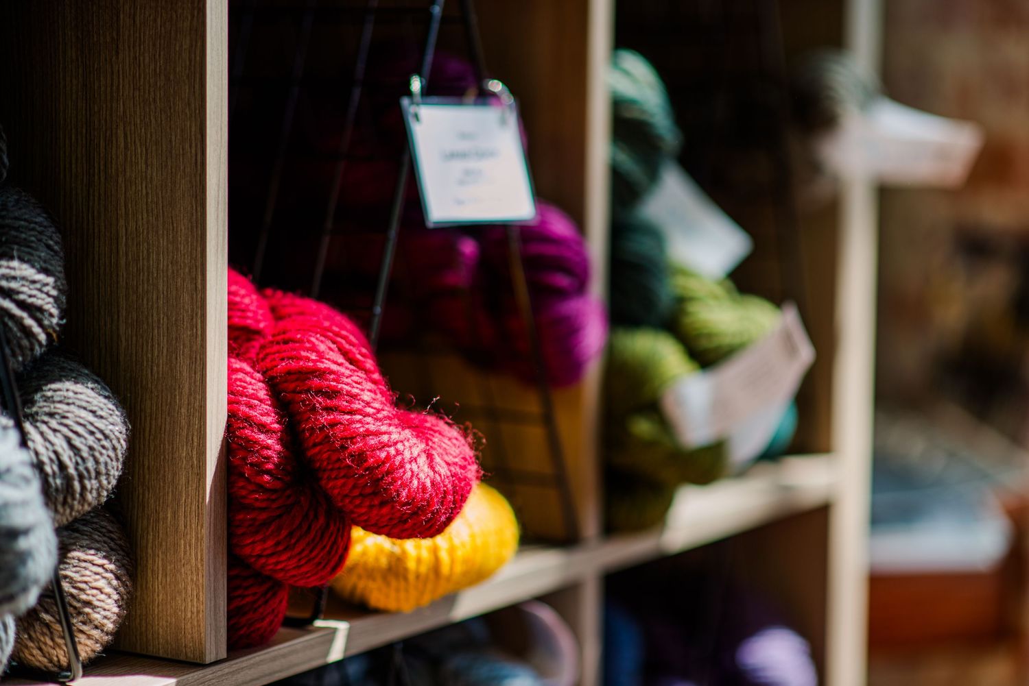 Colorful skeins of yarn displayed on wooden shelves with a price tag in a craft store.