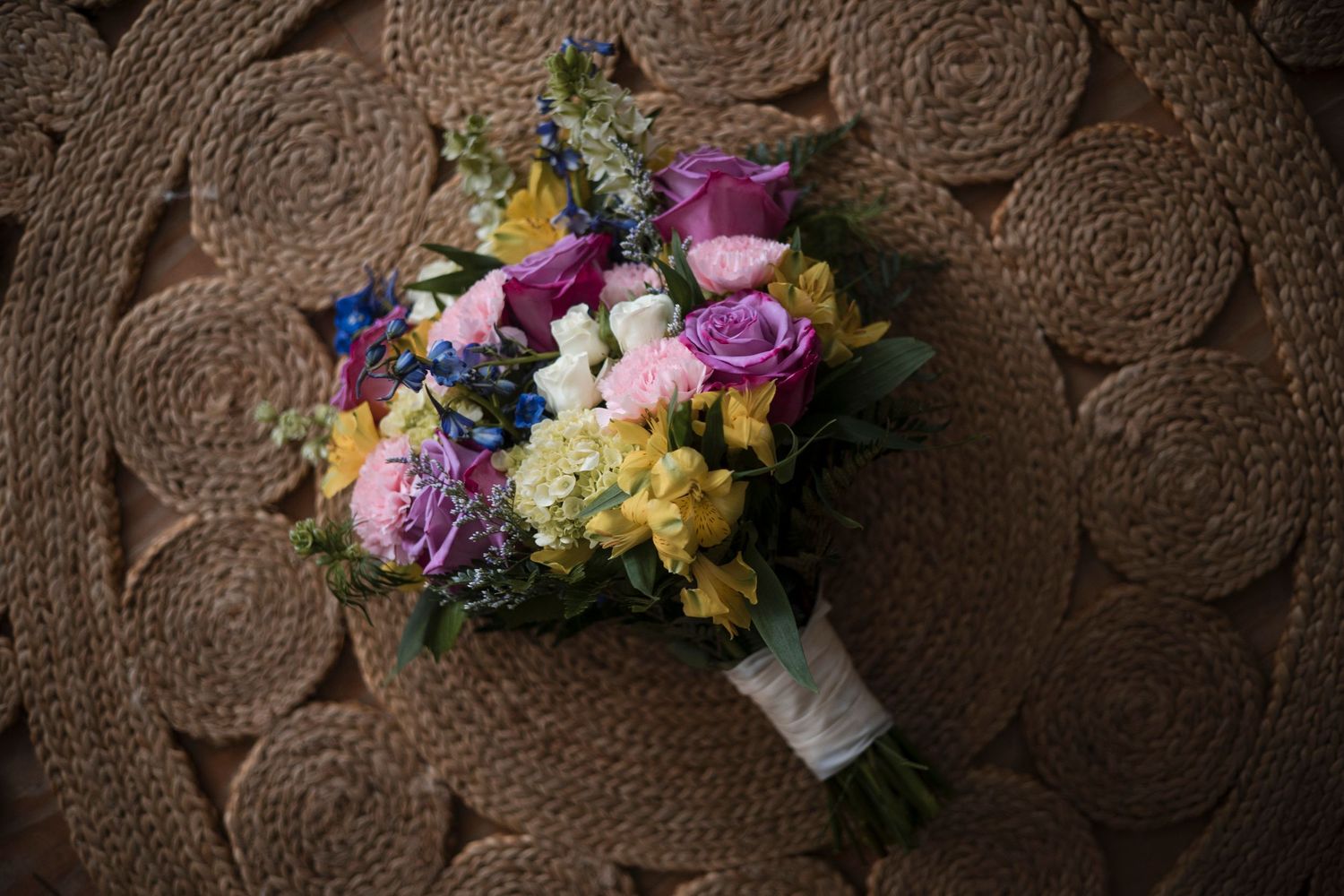 A bouquet of colorful flowers including purple, yellow and white blooms arranged on a textured brown background.