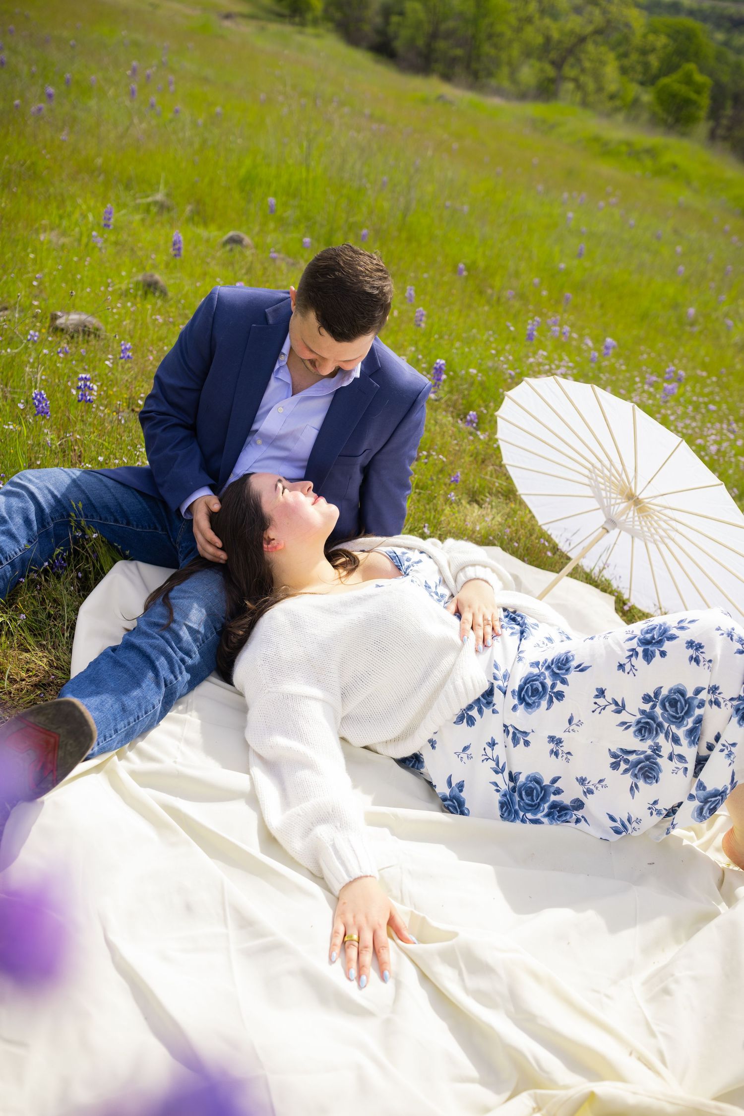 Romantic couple lying on blanket in flowering meadow with white parasol on sunny afternoon.