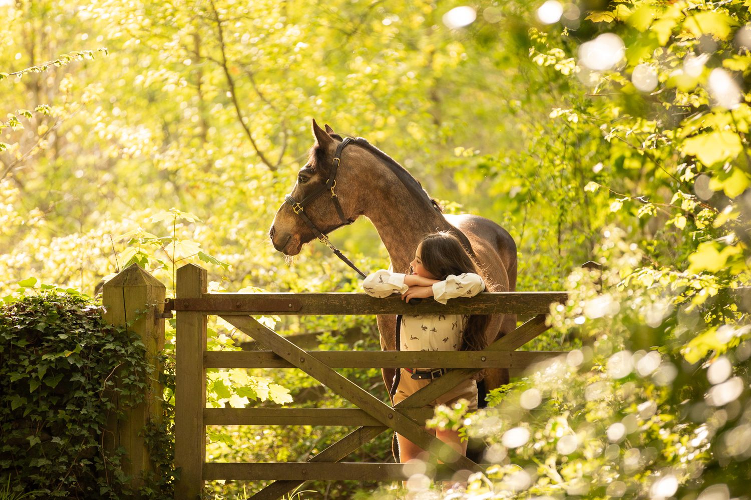Two riders stand with their animals - a dog and a dark horse relaxing outdoors in a black and white photo.