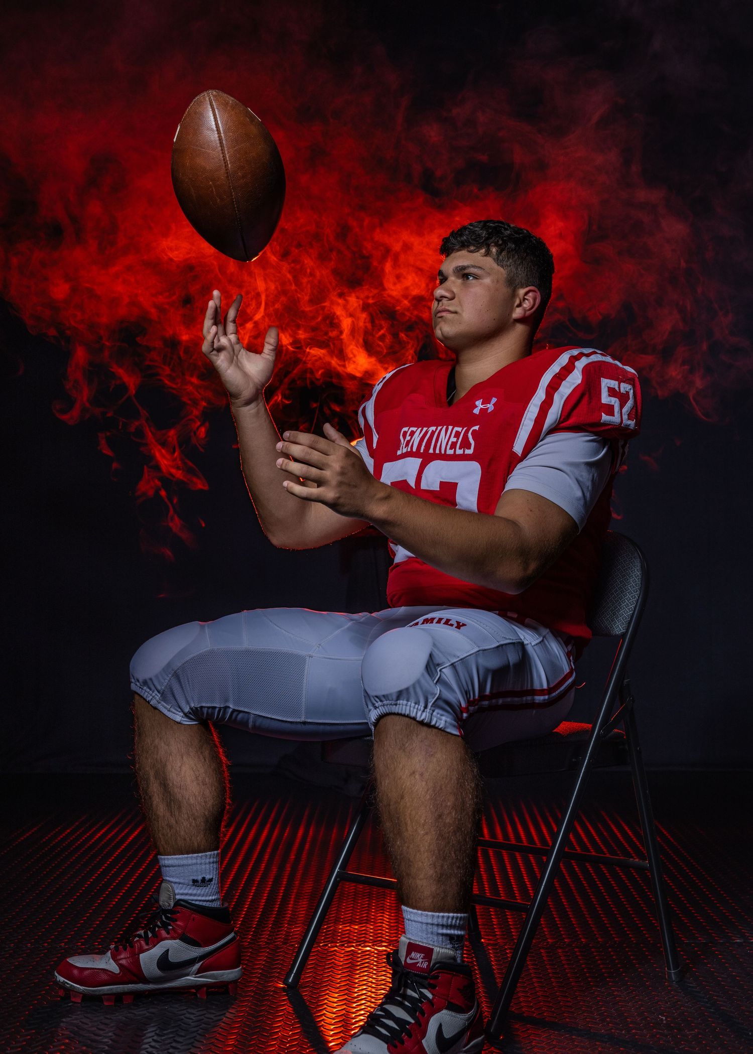 Football player in red uniform sitting on chair with dramatic lighting and smoke effects.