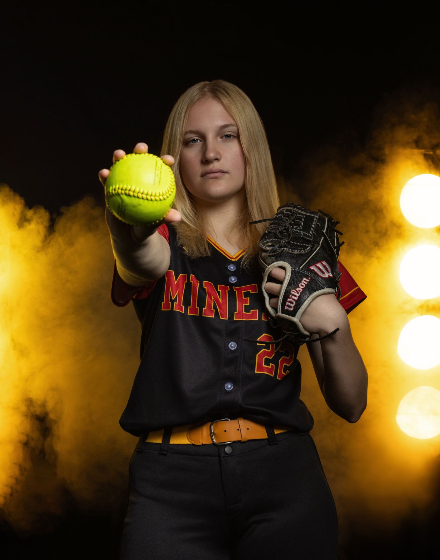 Softball player poses with equipment against dramatic yellow smoke background.