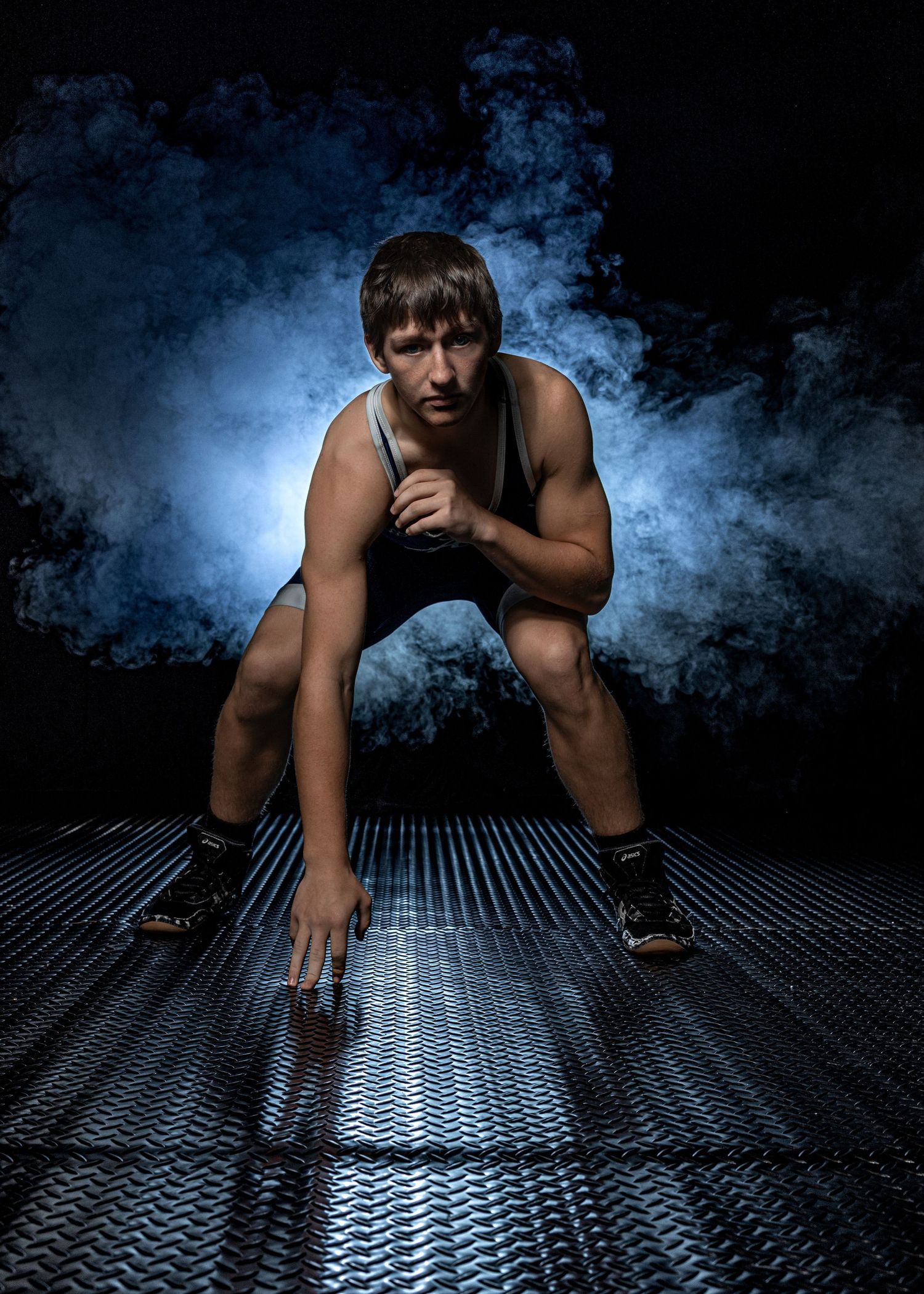 Athletic figure in dramatic pose on metal surface with moody blue smoke effects.