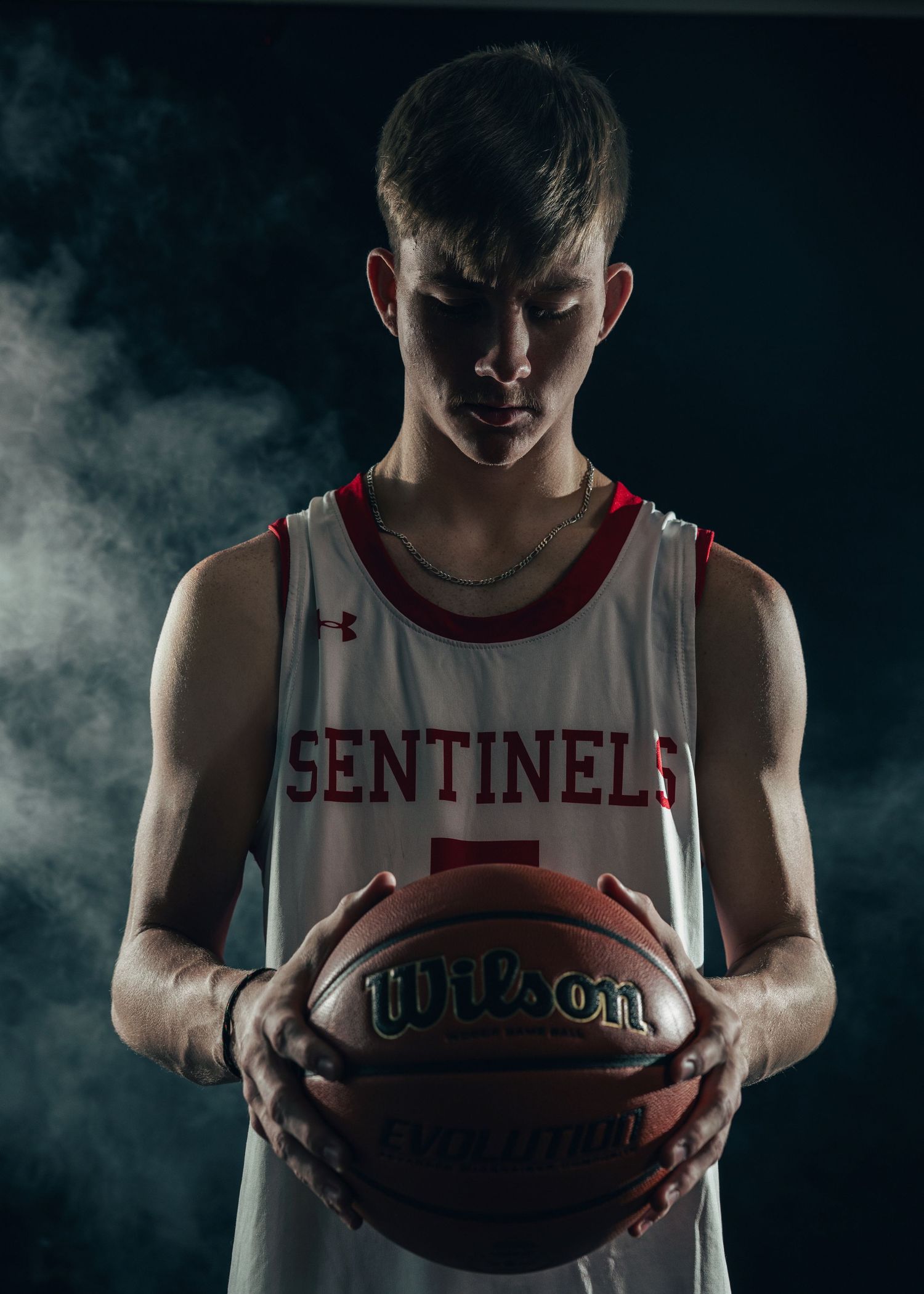 Basketball players hold Wilson basketballs in dramatic smoky lighting against dark background.