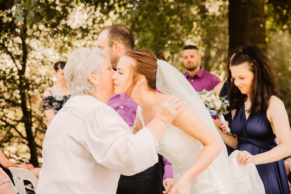 A touching moment shared between someone in a formal ivory dress and a person in light colored clothing at an outdoor gathering.