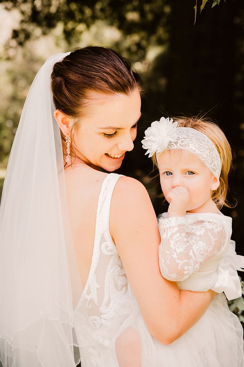 A tender wedding moment features white lace dresses and a flowing veil in warm golden sunlight.