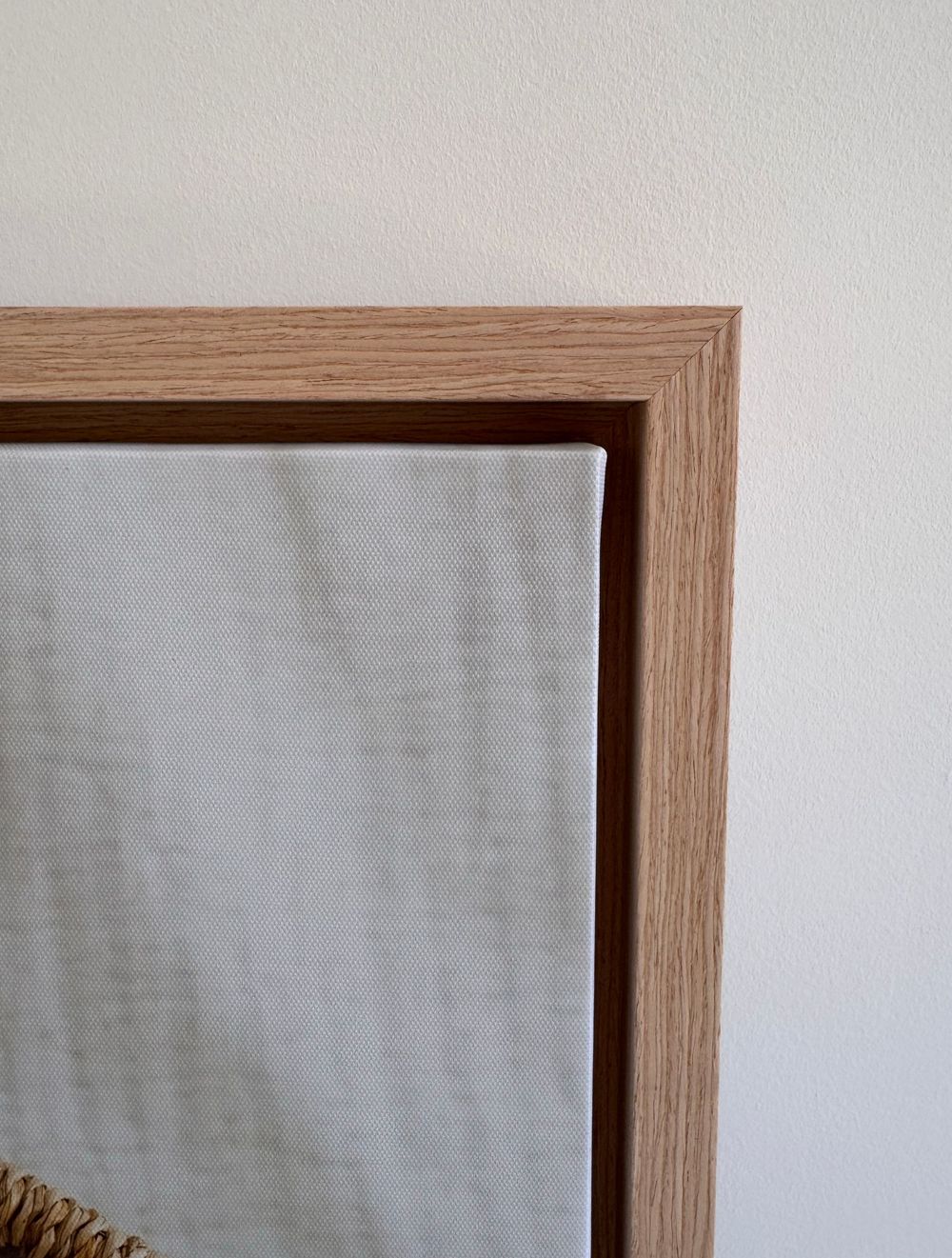 Close-up view of wooden picture frame corner mounted on white wall showing light oak grain detail.