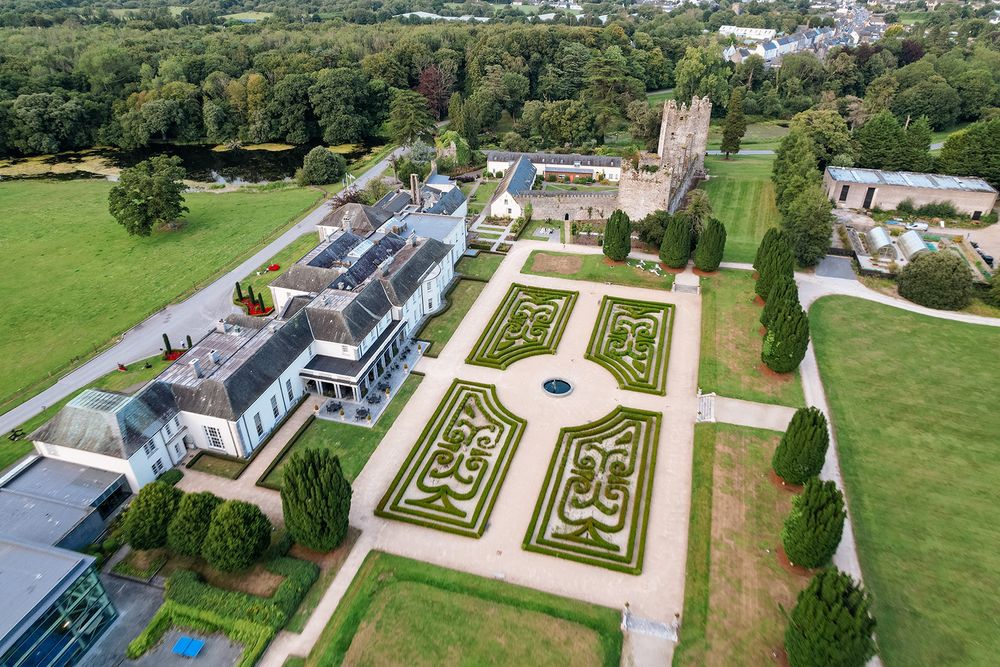Aerial panoramic view of a formal garden with manicured hedges and paths alongside an elegant mansion estate Castlemartyr Resort