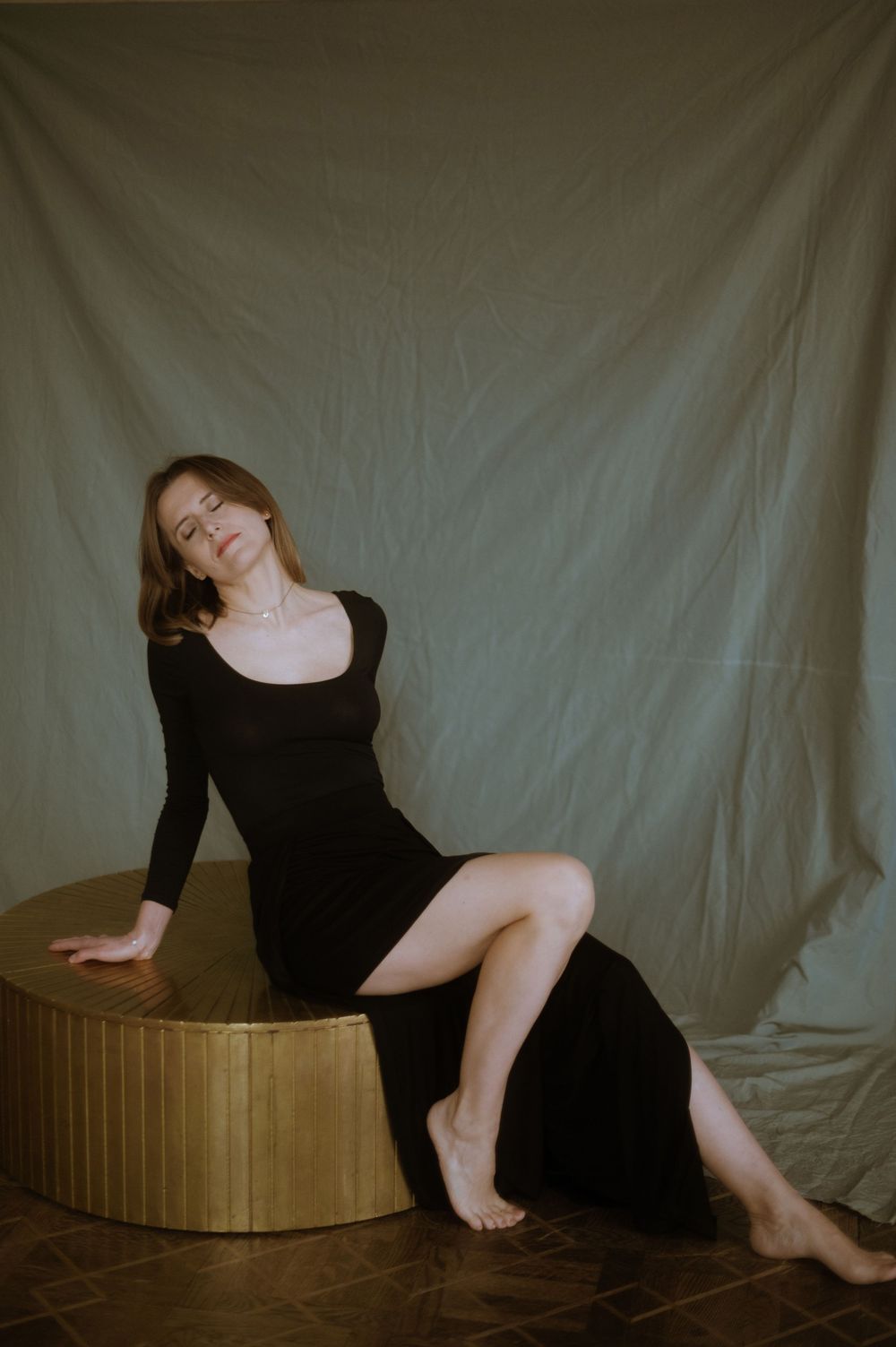 Artistic figure in black dress posing on wooden platform against white backdrop in sequential movement study.