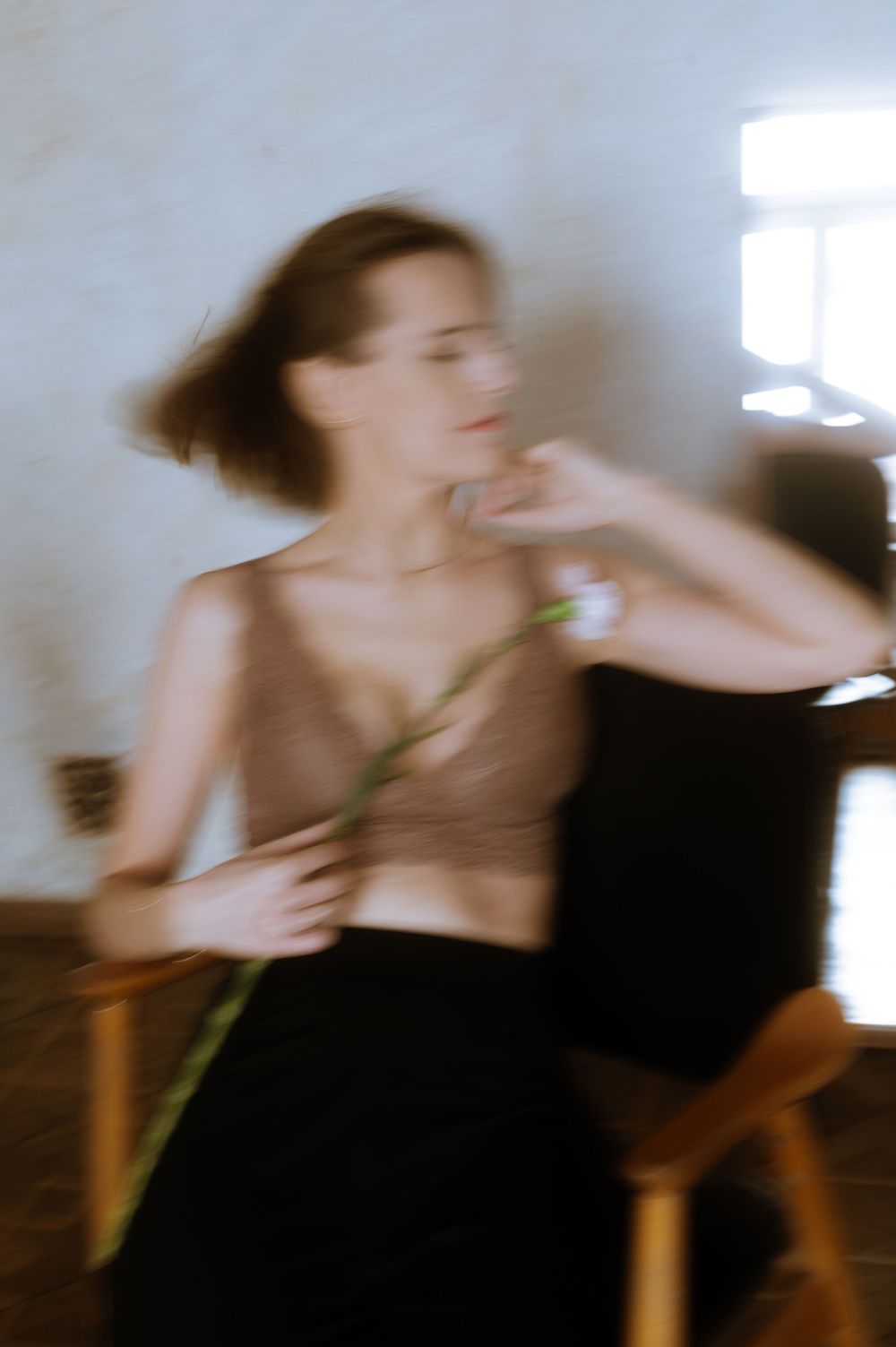 Artistic motion blur portrait with someone holding a flower in soft window light.