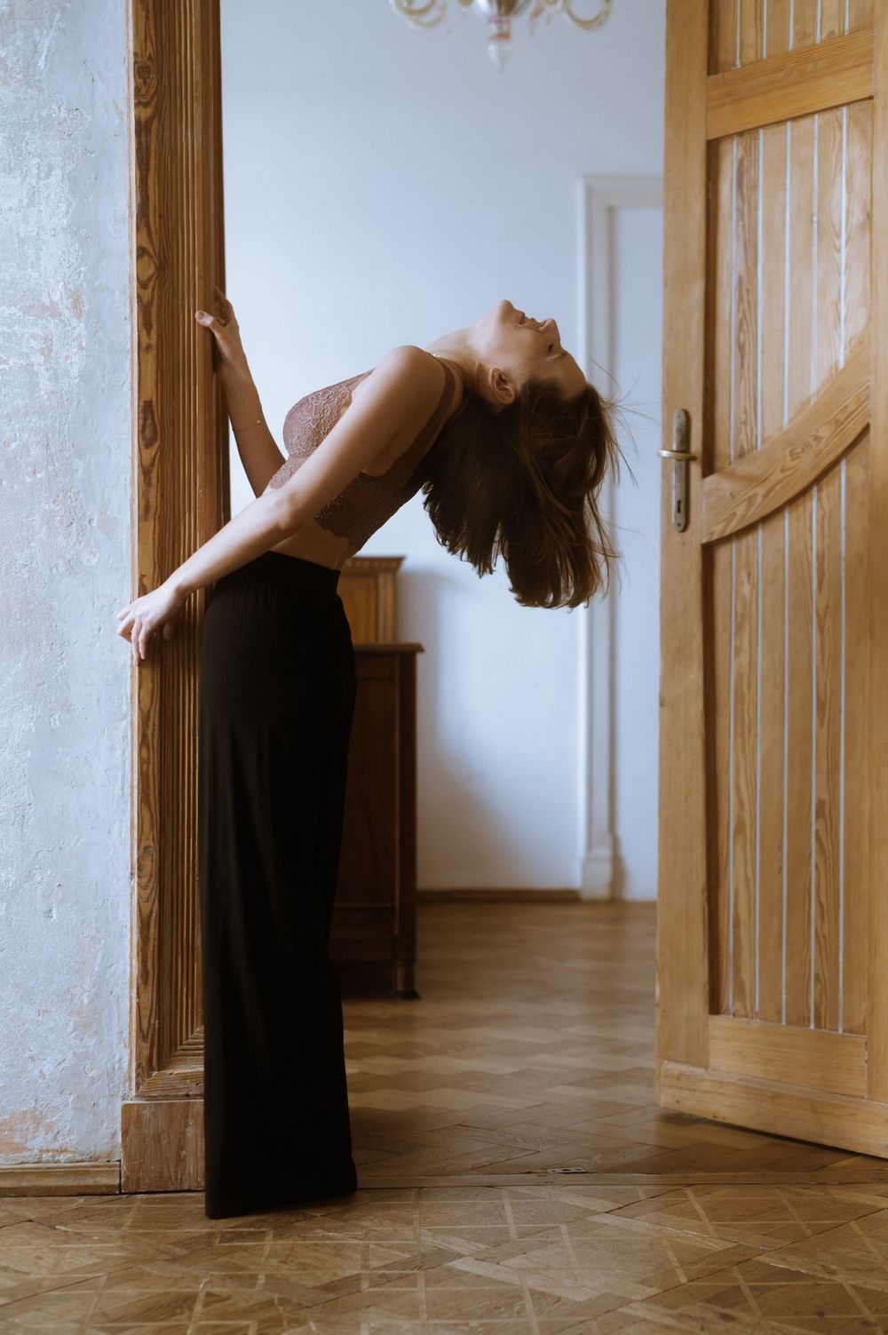 Graceful figure in black dress bending backwards in hallway with wooden doors.