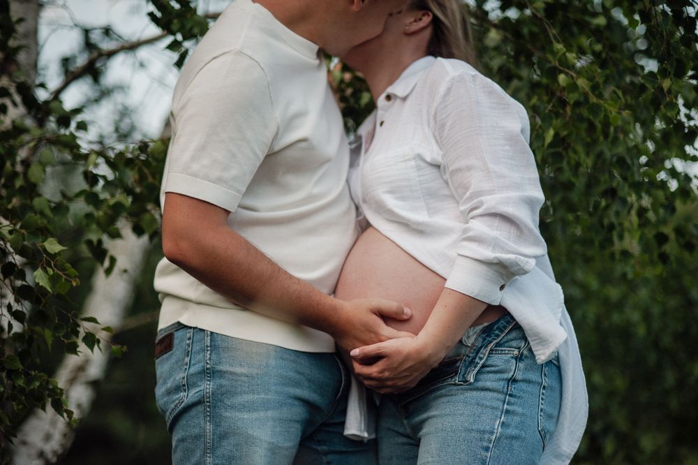 An intimate maternity photo of a couple in casual attire outdoors.