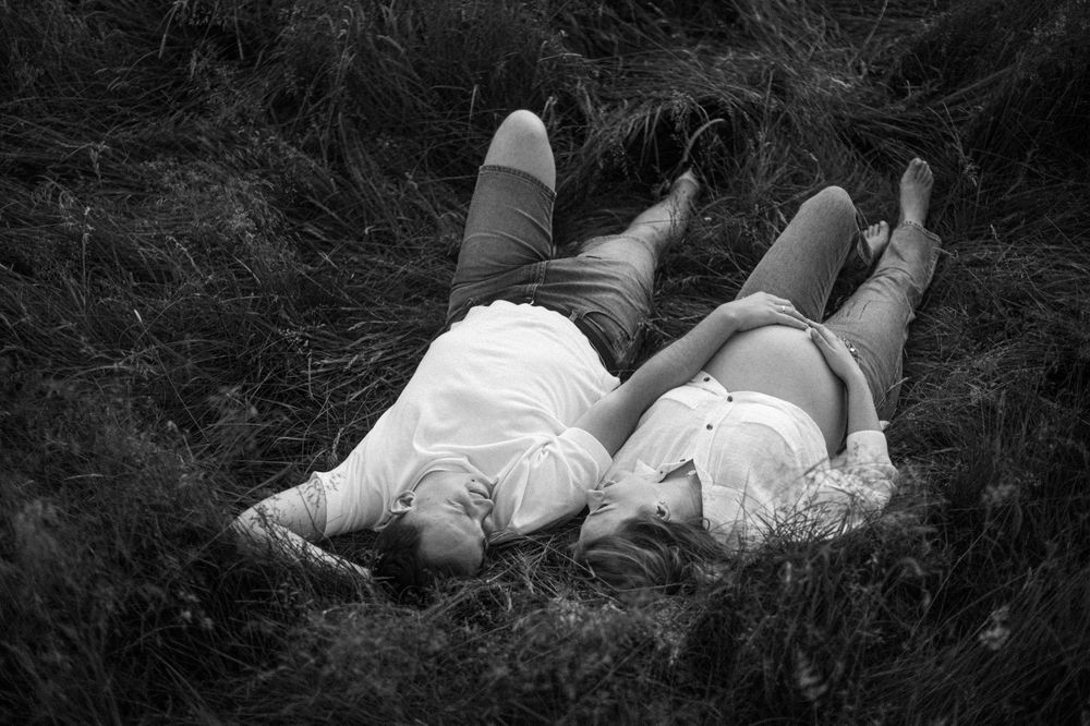 A black and white photo of two people lying in grass, creating a romantic outdoor scene.
