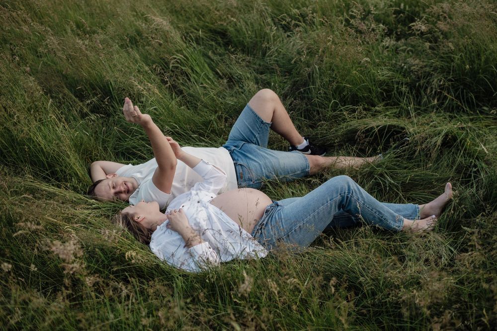 A couple lying in tall grass together on a sunny day, enjoying a romantic moment outdoors.