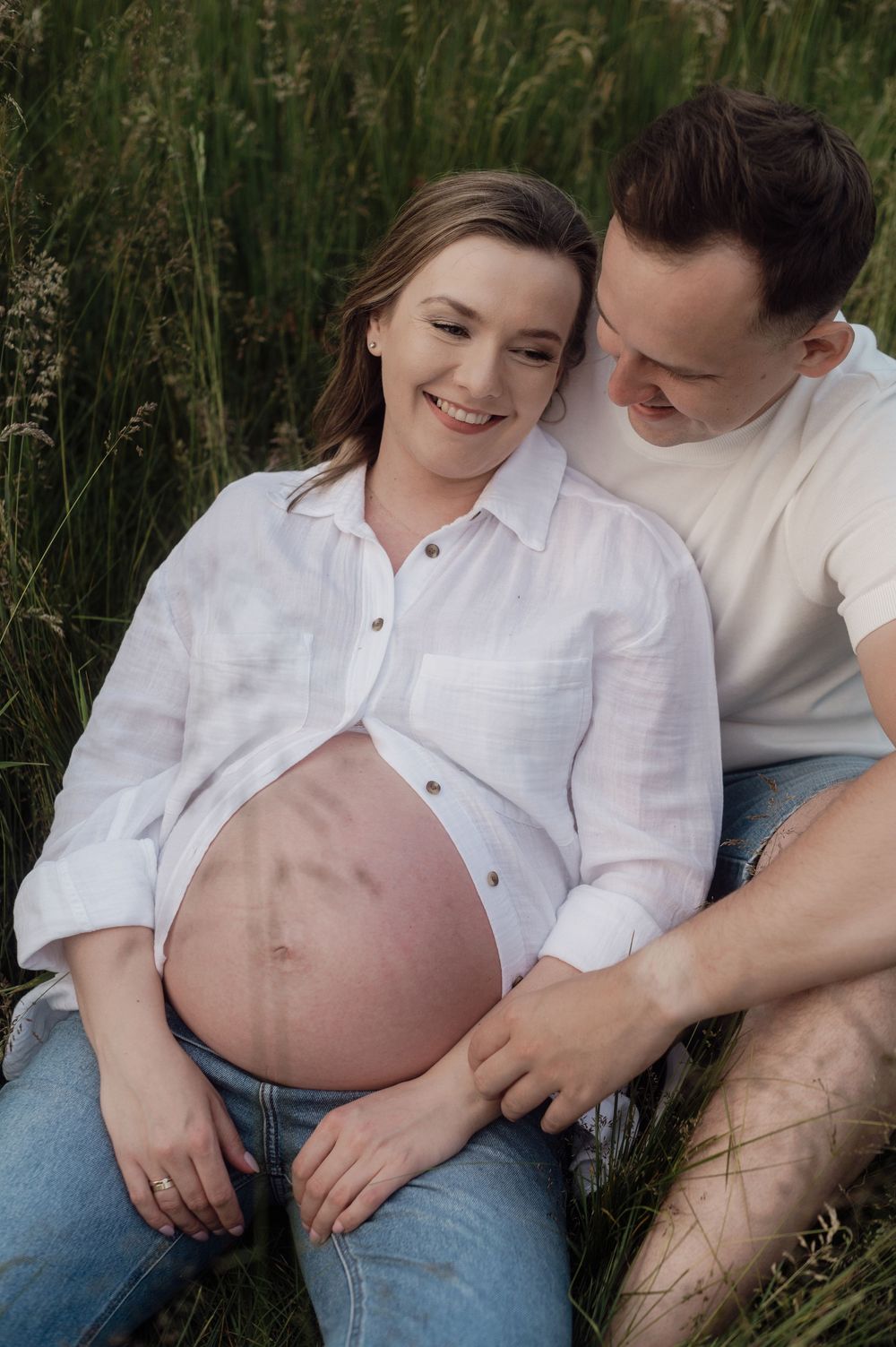 An intimate maternity photo of an expectant couple sitting in a field of tall grass.