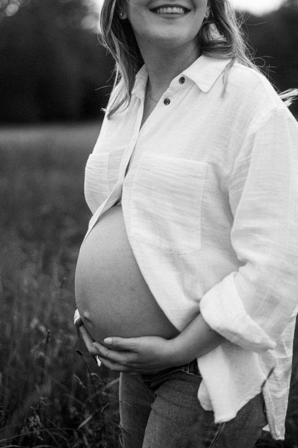 Black and white maternity photo showing pregnant belly with white button-up shirt and jeans.