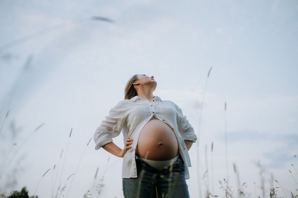 Maternity photo of pregnant belly against blue sky with tall grass in foreground.