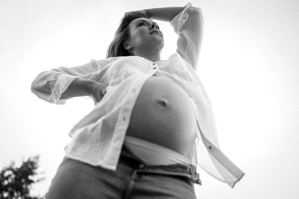 Low angle black and white photo showing pregnant belly with open white shirt.