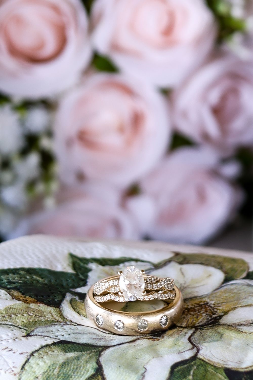 Gold wedding rings with diamonds displayed on floral dish with blush roses in background.