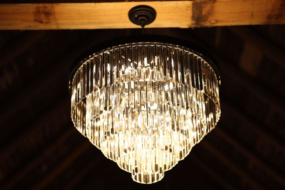 Elegant crystal chandelier with tiered glass prisms glowing warmly against a rustic wooden ceiling.
