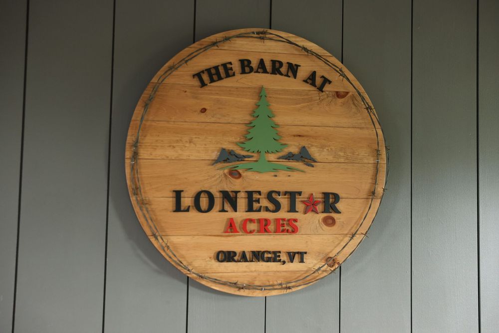 Rustic wooden barrel sign reading The Barn at Lone Star Acres Orange VT with pine tree logo.