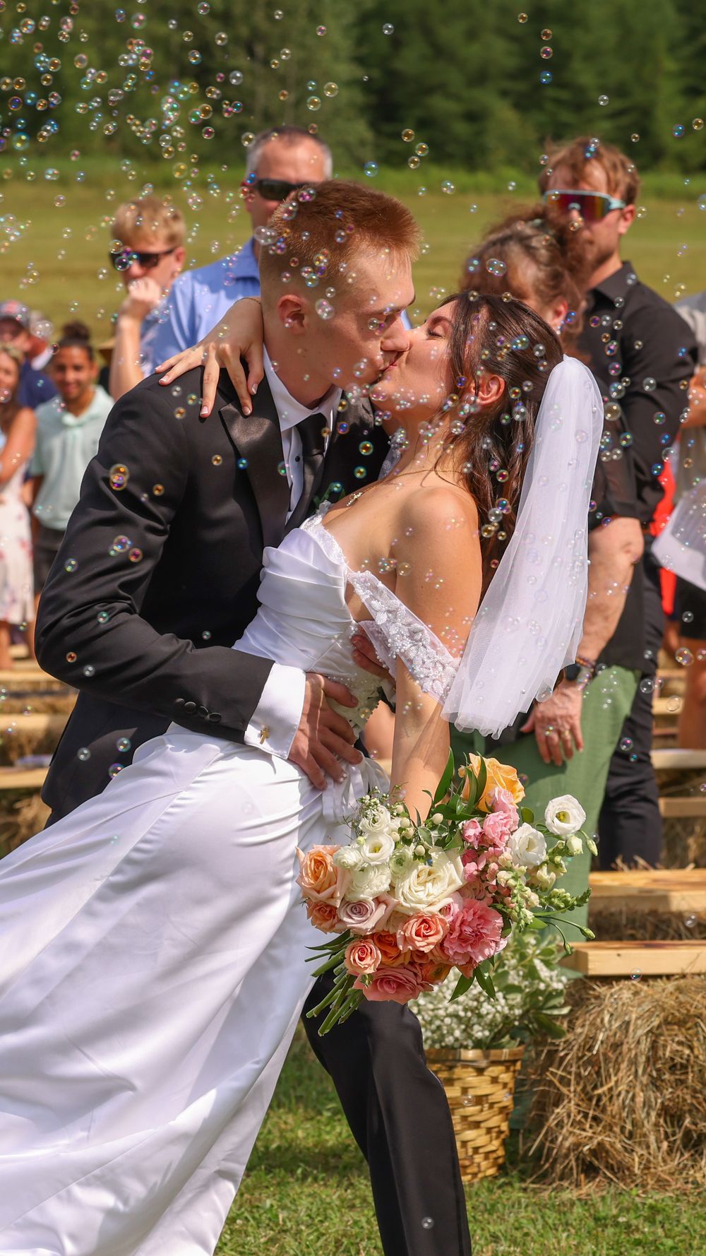 Bride and groom sharing a passionate kiss surrounded by bubbles while guests celebrate their wedding.