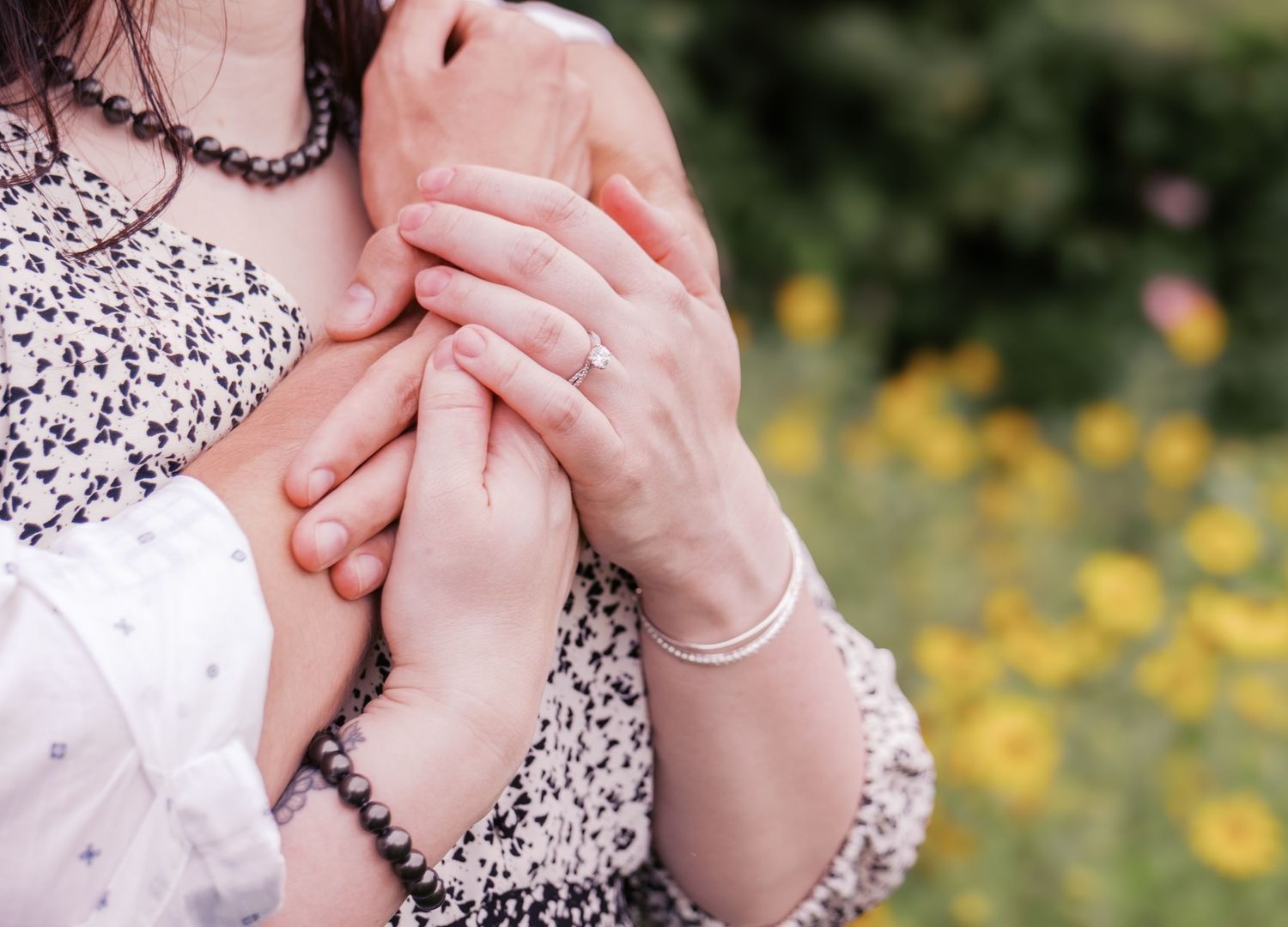 Close-up of hands tenderly clasped together against a floral patterned dress.