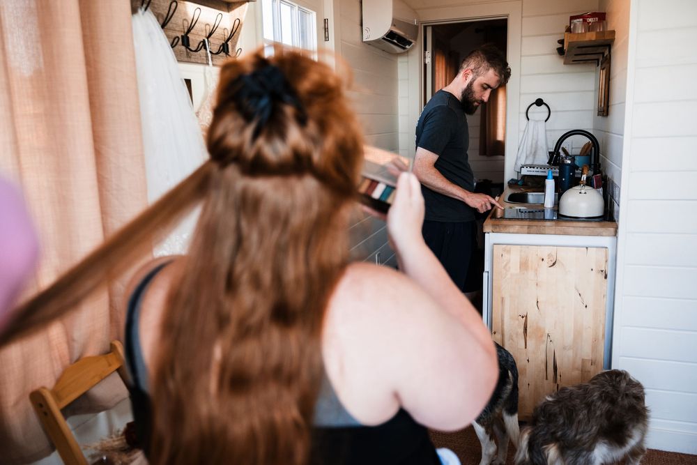 Two people interacting in a casual kitchen setting as one gestures with long brown hair flowing.