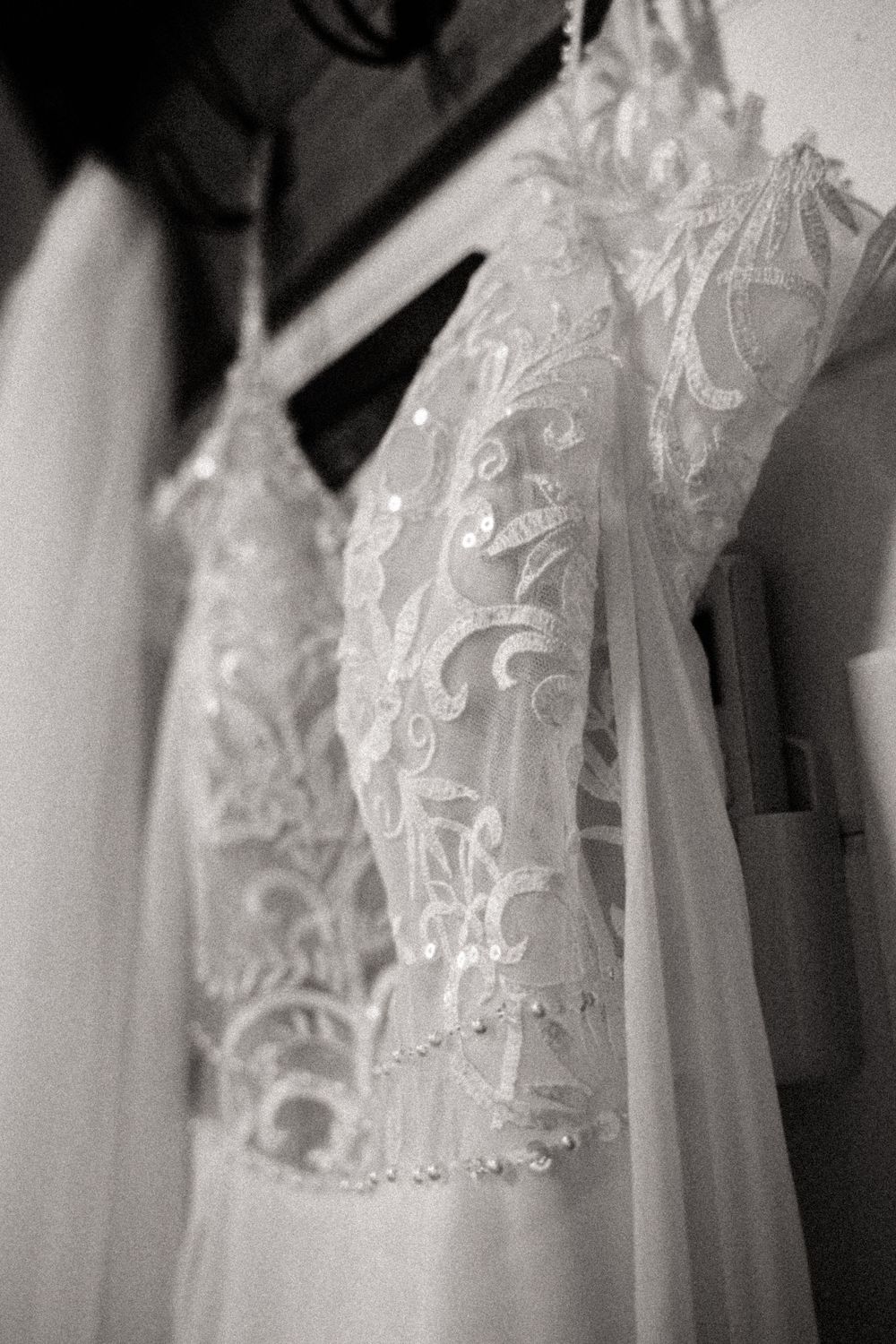Row of delicate white lace wedding dresses with intricate embroidery details hanging on black hangers.