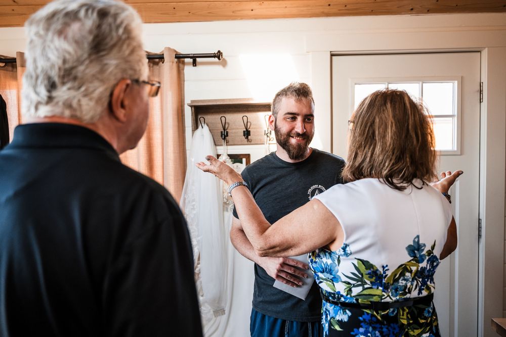 Three people having an animated conversation while standing in a home interior with wooden walls and white door.