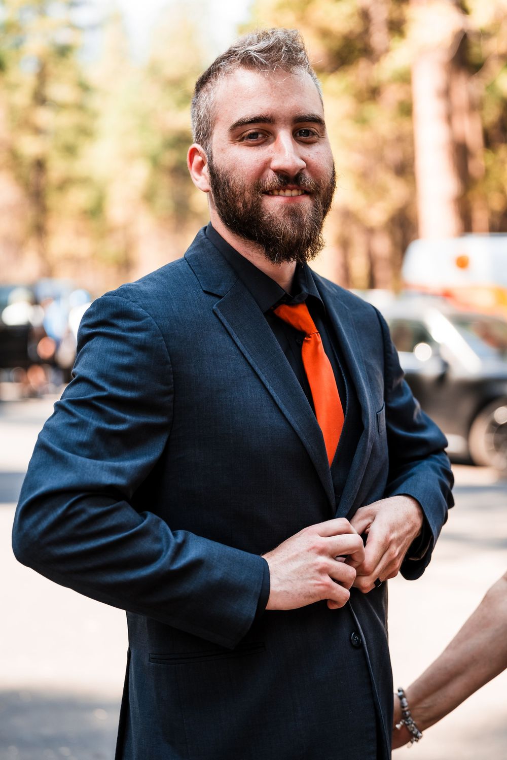 A sequence of photos showing a person in a navy suit and orange tie adjusting their outfit while standing outdoors.