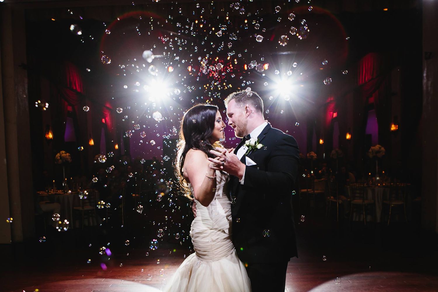 A couple shares a romantic dance moment on a dark dance floor surrounded by glowing lights and sparkles.