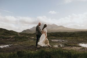 Couple in wedding attire standing together against stunning mountain landscape in Scottish Highlands.