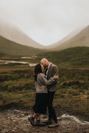 A romantic moment captured between a couple in the misty Scottish Highlands with rolling green hills in the background.