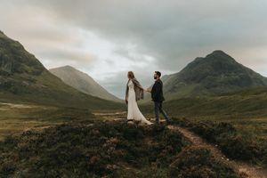 Wedding couple walks together through misty Scottish Highlands during golden hour photography session.